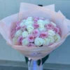 A woman gracefully holds a bouquet of pink and white roses, showcasing the beauty of the flowers in her hands.