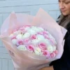 A woman gracefully holds a bouquet of pink and white roses, showcasing the beauty of the flowers in her hands.