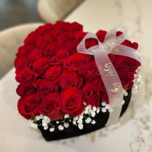 A heart-shaped box filled with vibrant red roses and delicate baby's breath, symbolizing love and affection.