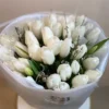 A bouquet of white tulips elegantly arranged on a wooden table, showcasing their delicate petals and fresh greenery.