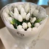 A bouquet of white tulips elegantly arranged on a wooden table, showcasing their delicate petals and fresh greenery.