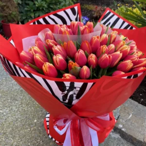 A vibrant bouquet of red and pink tulips elegantly tied with a stylish zebra print ribbon, showcasing a striking floral arrangement.