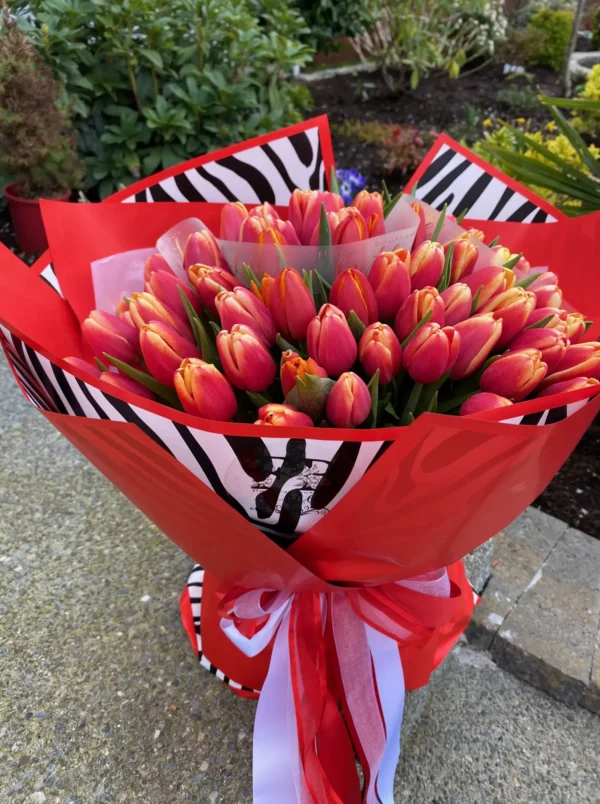 A vibrant bouquet of red and pink tulips elegantly tied with a stylish zebra print ribbon, showcasing a striking floral arrangement.