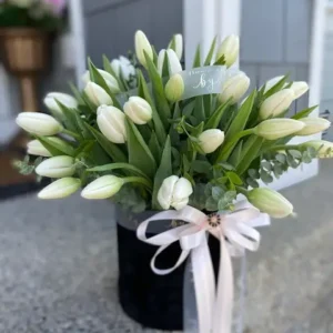 A bouquet of elegant white tulips arranged in a sleek black vase, showcasing a striking contrast of colors.