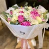 A vibrant bouquet of assorted flowers elegantly arranged in a simple white paper bag, showcasing natural beauty.