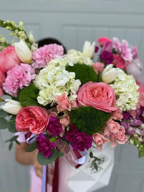 A woman gracefully holds a white box adorned with pink and white flowers, showcasing a delicate floral arrangement.