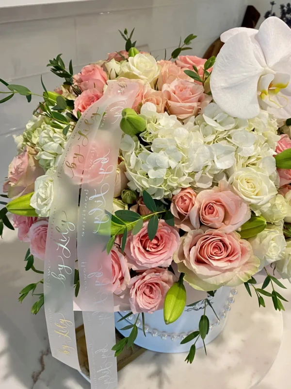 A white box adorned with delicate pink roses and elegant orchids, creating a charming floral arrangement.