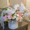 A white box adorned with delicate pink roses and elegant orchids, creating a charming floral arrangement.