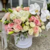 A white box adorned with delicate pink roses and elegant orchids, creating a charming floral arrangement.