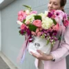 A woman gracefully holds a white box adorned with pink and white flowers, showcasing a delicate floral arrangement.