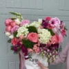 A woman gracefully holds a white box adorned with pink and white flowers, showcasing a delicate floral arrangement.